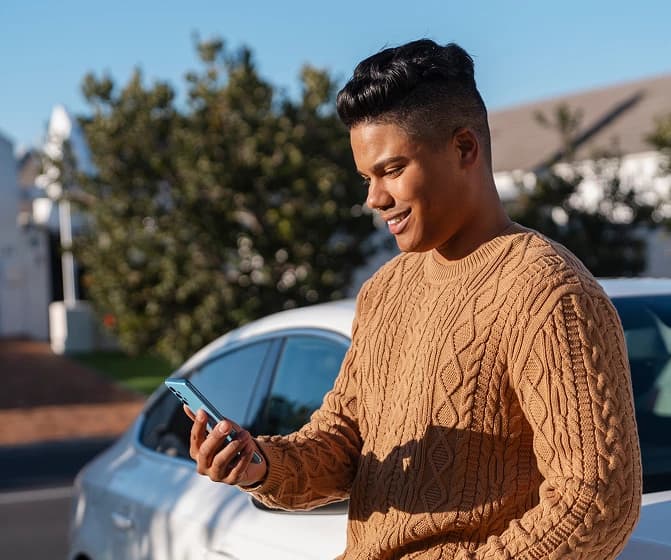 Homem sorridente encostado no carro enquanto navega pelo aplicativo Reuel
